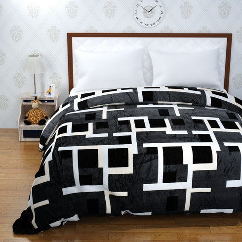 A bed with a black and white geometric patterned blanket, with a white pillow and a wooden headboard against a white wall, with a clock above the headboard.