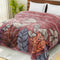 A double bed with a multicolored floral blanket spread over it, with a pink, orange, and gray color scheme.