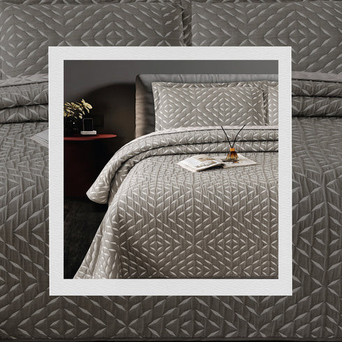 A bed covered with a gray jacquard bedcover set with a geometric pattern, including two pillow covers, in a bedroom setting.
